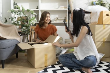 Konforlu Salon 'da taşınma kutularını açan iki Asyalı kadın akıllı telefondan listeyi kontrol ediyor. Mutlulukla konuşuyorlar.