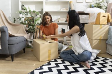 Konforlu Salon 'da taşınma kutularını açan iki Asyalı kadın akıllı telefondan listeyi kontrol ediyor. Mutlulukla konuşuyorlar.