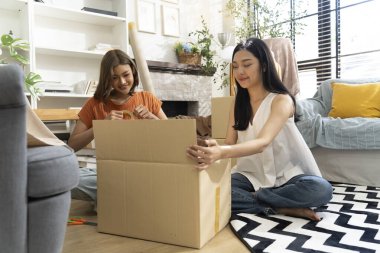 İki genç Asyalı kadın yaşam alanına karton kutuları neşeyle açıyor, bitkiler ve doğal ışıkla çevrili, dostluk ve keşif anı sergiliyorlar, birlikte konuşuyorlar ve mutlu bir şekilde gülümsüyorlar.