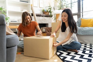 İki genç Asyalı kadın yaşam alanına karton kutuları neşeyle açıyor, bitkiler ve doğal ışıkla çevrili, dostluk ve keşif anı sergiliyorlar, birlikte konuşuyorlar ve mutlu bir şekilde gülümsüyorlar.