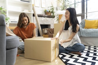 İki genç Asyalı kadın yaşam alanına karton kutuları neşeyle açıyor, bitkiler ve doğal ışıkla çevrili, dostluk ve keşif anı sergiliyorlar, birlikte konuşuyorlar ve mutlu bir şekilde gülümsüyorlar.