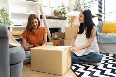 İki genç Asyalı kadın yaşam alanına karton kutuları neşeyle açıyor, bitkiler ve doğal ışıkla çevrili, dostluk ve keşif anı sergiliyorlar, birlikte konuşuyorlar ve mutlu bir şekilde gülümsüyorlar.