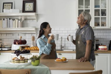 Asyalı, gülümseyen son sınıf çifti modern bir mutfakta kahvelerini yudumlarken ellerinde sıcak bir içecek tutuyorlar ve birlikte konuşmaktan zevk alıyorlar. Olgun çiftler evlerinde mutluluğu paylaşırlar.