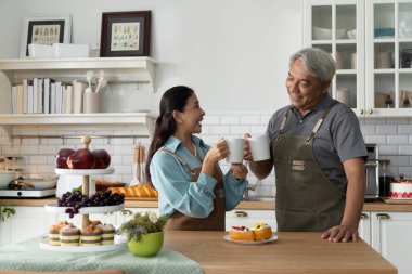 Asyalı, gülümseyen son sınıf çifti modern bir mutfakta kahvelerini yudumlarken ellerinde sıcak bir içecek tutuyorlar ve birlikte konuşmaktan zevk alıyorlar. Olgun çiftler evlerinde mutluluğu paylaşırlar.