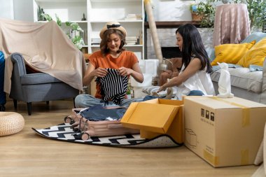 İki güzel kadın, parlak, dekore edilmiş oturma odasında kutuları taşıyan bir bavulu boşaltıp yeni bir ev dekore etmeye hazırlanıyorlar, konuşuyorlar ve birlikte mutlulukla gülümsüyorlar.