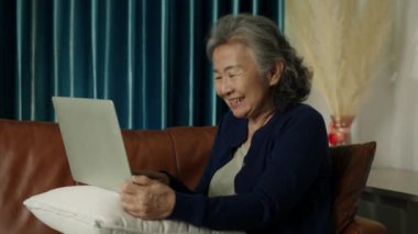 Orta boy, mutlu Asyalı olgun kadın oturma odasındaki kanepede dizüstü bilgisayar kullanıyor. Online televizyon seyreden son sınıf öğrencisi bir bayan ya da internetten arkadaşlarıyla sohbet eden komik biri..