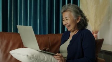 Kilitli atış, Amigoluk yapan Asyalı olgun kadın evdeki kanepede dizüstü bilgisayar kullanıyor. Online TV izleyen son sınıf öğrencisi bayan gülmek ya da sanal toplantı yapmak, internet üzerinden sohbet etmek..