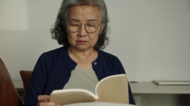 Görüntüler kilitli, ciddi, olgun bir kadının gözlük takıp evde dinlenirken kitap okuduğu yüz ifadesi..
