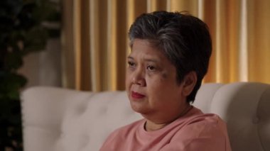 Video görüntüleri yakın çekim, Asya 'lı yaşlı bir kadının kısa saçlı, gözyaşlarını silen ve oturma odasında yalnız başına hüzünlü bir film sahnesini izlerken burnundan akan bir mendille görüntüler..