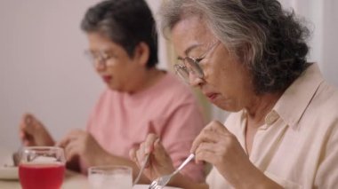 Görüntüler, orta boy, seçici odaklanma, gözlüklü iki yaşlı kadın oturup lezzetli yemekler yiyor, tartışarak ve eğlenerek birlikte gülüyorlar.