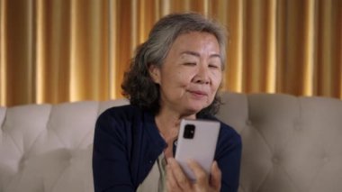 Görüntüler kilitli oturma odasında akıllı telefonlu müzik dinleyen neşeli Asya 'lı son sınıf öğrencisi Mutlulukla cep telefonuna bakarken şarkı söylemekten hoşlanıyor.