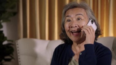 Görüntüler kilitli, neşeli, son sınıf öğrencisi bir kadının gülümsemesi oturma odasında sohbet ederken, yüz ifadeleri neşe ve mutluluğu ifade eder..