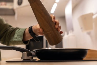 Female Hand pouring pepper into a frying pan on stove.  suggesting  preparation of  meal. The scene conveys a sense of home cooking and culinary activity. clipart