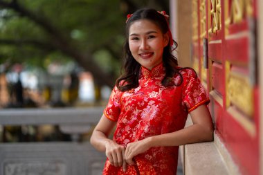 Güzel kırmızı Qipao giymiş gülümseyen kadının portresi geleneksel bir Çin tapınağının önünde elinde kırmızı bir mendille zarif bir şekilde duruyor. Geleneksel ay veya Çin Yeni Yıl kutlamaları 