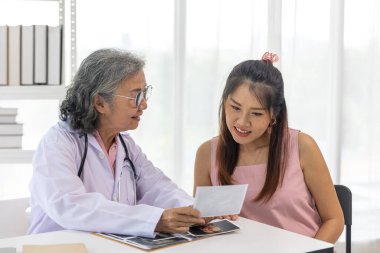 Kıdemli kadın doktor, hastanede doğum öncesi muayenesi sırasında gülümseyen hamile kadına ultrason görüntülerini açıklıyor.