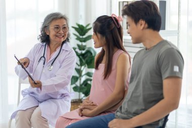 Seçici odaklanma, Kıdemli Meslek Doktoru hamile mutlu çifte danışmanlık ve anne adaylarının sağlığını tartışmak için dijital tablet kullanır. Genç çift neşeli ve nişanlı görünüyor.