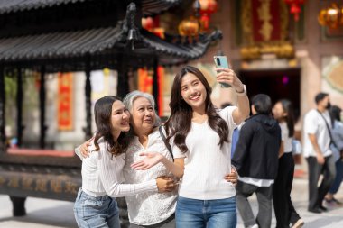 Çin Yeni Yıl kutlamaları sırasında Çin tapınağında fotoğraf çeken iki neşeli kız ve annenin portresi, mutlu bir şekilde gülümseyin.