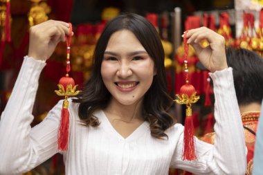 Genç Asyalı bir kadın Çin Yeni Yılı için güzel dekorasyon ürünlerini açık hava pazarında sergiliyor, kültürel alışveriş deneyiminin tadını çıkarıyor. Gülümse ve kameraya bak.