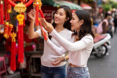 Genç Asyalı kadınlar Çin Yeni Yılı için açık hava pazarından güzel dekorasyon ürünleri satın alarak kültürel alışveriş deneyimlerinin tadını çıkarıyorlar..