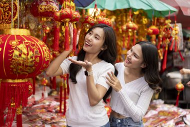 Neşeli genç Asyalı kadınlar Çin Yeni Yılı için açık hava pazarından güzel dekorasyon ürünleri satın alarak kültürel alışveriş deneyimlerinin tadını çıkarıyorlar..