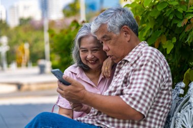 Parkta bankta oturan Asyalı yaşlı çift, bir anlık neşe ve bağlantı paylaşıyorlar, kocasının akıllı telefonunda ilginç bir şey, arkadaşlık ve hayatın basit zevkleri.