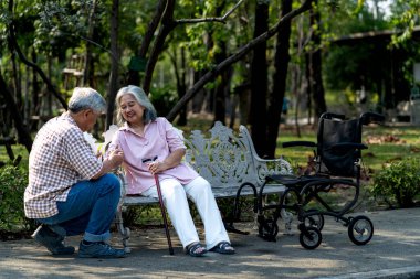Yaşlı bir çift güzel bir bankta oturmuş, birlikte huzurlu bir anın tadını çıkarıyorlardı. Kıdemli adam kadına bir şeyler fısıldamak için eğiliyor, karısı da ona sıcak bir şekilde gülümsüyor. Tekerlekli sandalye yakında.