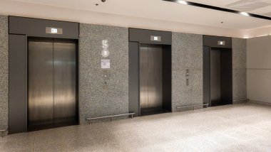 Granit duvarlara karşı paslanmaz çelik kapıları olan modern asansör lobisi. Minimalist tasarım, cilalı zemin ve iş ortamları için aydınlatılmış göstergeler.