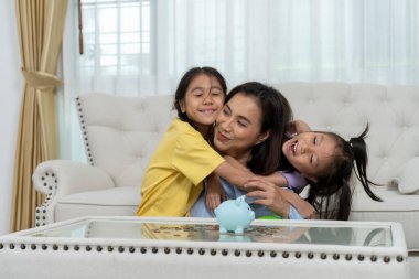 Bir aile evde birlikte para biriktirirken görülüyor, aileleri çocuklarına madeni paraları ve kumbarayı kullanarak finansal okur yazarlığı öğretiyor. Bu görüntü aile bağlarının ve eğitimin özünü yansıtır..