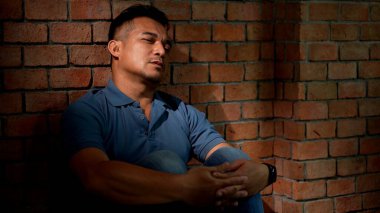 Ümitsiz adam tuğla duvara yaslanıyor, üzüntü, umutsuzluk, boş ya da derin düşünceler ifade ediyor, yüzünde güneş ışığı, yüz ifadesi kavramı