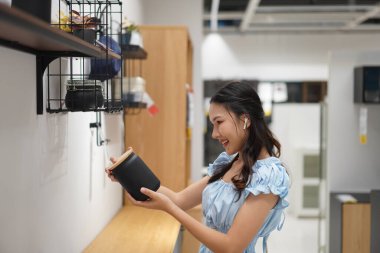 Modern mutfakta ya da mağazada, duvardaki siyah kavanoza uzanan kablosuz kulaklıklı genç Asyalı kadın, ev organizasyonunu ya da iç ürün kullanımını gösteren yaşam tarzı