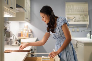 Asyalı kadın çekmecede ahşap mutfak gereçleri düzenliyor, düzenli mutfak malzemeleri, huzurlu ruh hali ve modern yaşam tarzı hazırlıyor.