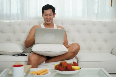 Adam dizüstü bilgisayarında muz yerken, kanepede bacak bacak bacak üstüne atarken eğleniyor..