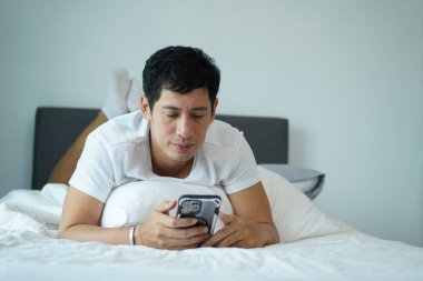 Asyalı adam telefona odaklanıp, sabahları dinlenirken karnının üstünde yatıyordu..