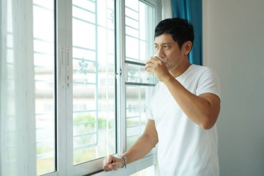 Beyaz gömlekli Asyalı adam soya sütü içiyor. Huzurlu bir sabah rutini. Evde sağlıklı bir yaşam sürüyor.