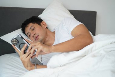 Adam akıllı telefon, sabah rutini ve dijital yaşam tarzı kullanarak yatakta yatıyor. Uyandıktan sonra telefon kontrol ediliyor..
