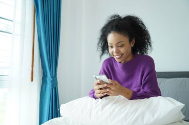 Beyaz battaniyeli akıllı telefon kullanırken gülümseyen genç Afrikalı kadın, günlük yaşam tarzı, konfor ve dijital bağlantı gösteriyor