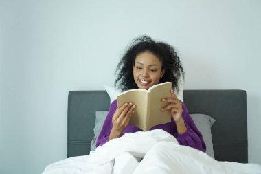 Mutlu Afrikalı kadın kitap okurken gülümsüyor. Sıcak bir sabah, doğal ışık ve sakin bir hava ile.