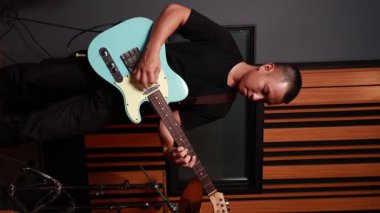 Profesyonel müzik stüdyosunda mavi elektro gitar çalan odaklanmış Asyalı erkek müzisyen, mobil içerik, müzik tanıtımı ve yaratıcı editoryal kullanım için ideal dikey format