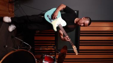 Asyalı erkek müzisyen, profesyonel müzik stüdyosunda dikey ahşap duvar ile mavi elektro gitar çalarken, müzik içeriği oluşturmak için modern kapalı ortam