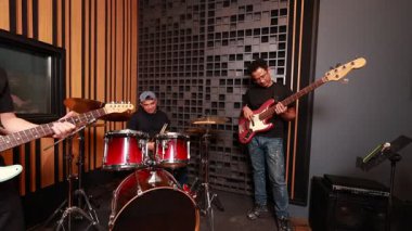 Ses geçirmez stüdyodaki Asyalı erkek müzisyenler, modern müzik ortamında takım çalışmasını, baskıyı ve yaratıcılığı ifade ederek, yorgunluk ve canlı performans anlarını gösteriyorlar.