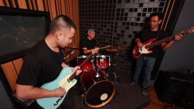 Ses geçirmez stüdyoda elektronik gitar, davul ve bas çalan Asyalı erkek müzisyenler, modern müzik yaşam tarzı ve yaratıcılığını temsil eden performans ve takım çalışmasına odaklandılar.