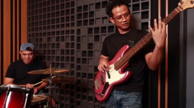 İki Asyalı müzisyen ses geçirmez odada şarkı söylüyor, biri kırmızı elektro gitar çalıyor, biri davul çalıyor, odaklanmış ve ciddi, stüdyo ortamında, yaşam tarzında.