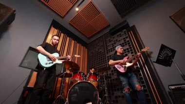 Ses geçirmez stüdyoda gitar, bas ve davul çalan üç Asyalı erkek müzisyen, canlı performans ve takım çalışmasının alçak ve ön açılarını kaydediyor.