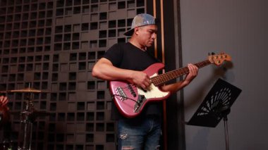 Profesyonel akustik stüdyoda elektronik gitar, bas ve davul çalan Asyalı erkek orkestra üyeleri, enstrümanlarla çalgıcılar arasında kamera görüntüsü