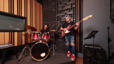 Profesyonel ses geçirmez stüdyoda elektro gitar, bas ve davul çalan üç Asyalı erkek müzisyen birlikte müzik yapmaya odaklandılar.