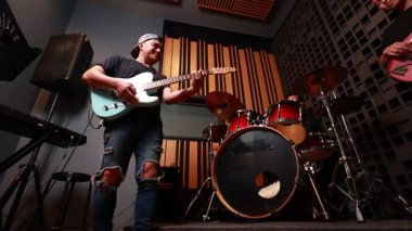 Profesyonel stüdyoda elektro gitar, bas ve davul çalan üç Asyalı genç adam, düşük açıdan, sıcak ışıktan, anlamlı titreşimlerden, canlı müzik performansına odaklanıyor.