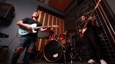 Profesyonel ses geçirmez stüdyoda elektronik gitar, bas ve davul çalan üç Asyalı genç adam müzikten, gündelik kıyafetlerden, modern enstrümanlardan ve sıcak aydınlatmadan keyif alıyorlar.