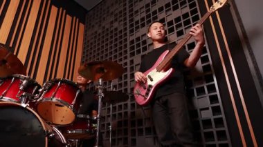 Profesyonel kayıt stüdyosunda davul çalan iki genç Asyalı adam, müzik, sıcak ışık, siyah tişörtler ve ses geçirmez modern duvar performanslarına odaklanmış.