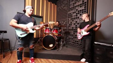 Profesyonel ses geçirmez stüdyoda birlikte çalan üç Asyalı ön planda elektro gitarist arka planda baterist ve bas gitarist odaklanmış ve enerjik bir prova oturumu.