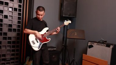 Asyalı genç adam profesyonel ses geçirmez stüdyoda gitar çalarken odaklanıyor. Prova için hoparlör ve amplifikatörün yanında duruyor.